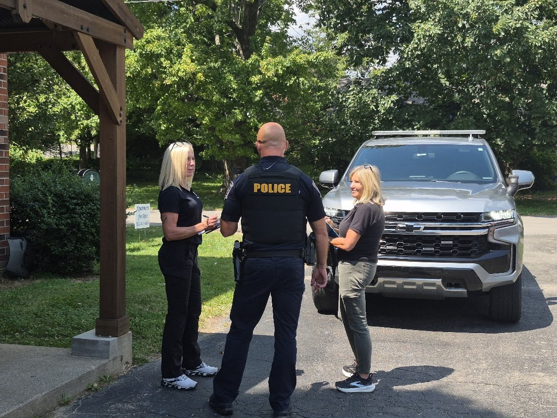 Two REACH staff members speaking with a Jeffersontown police officer beside a police vehicle